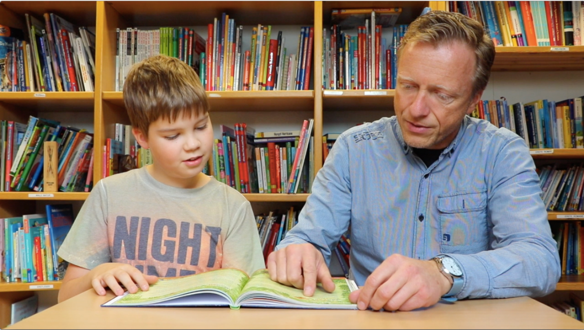 Schüler und Lehrer lesen gemeinsam aus einem Buch
