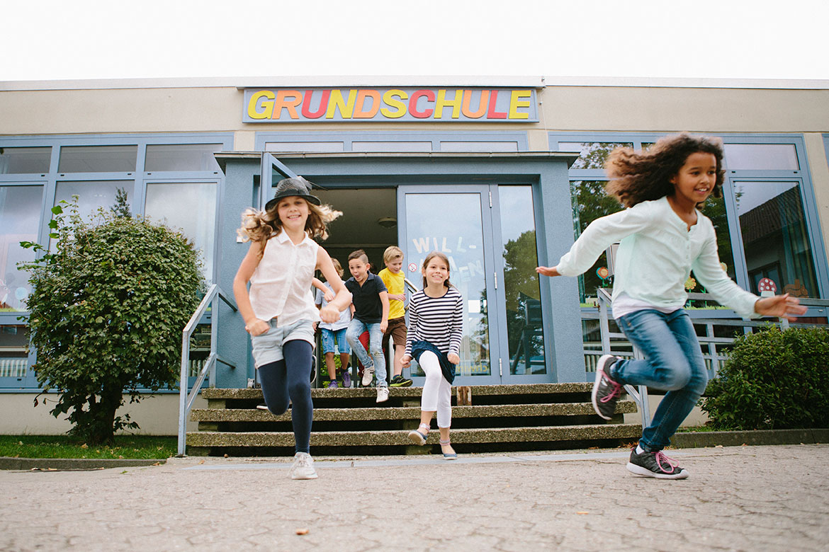 Kinder laufen fröhlich aus dem Schulgebäude